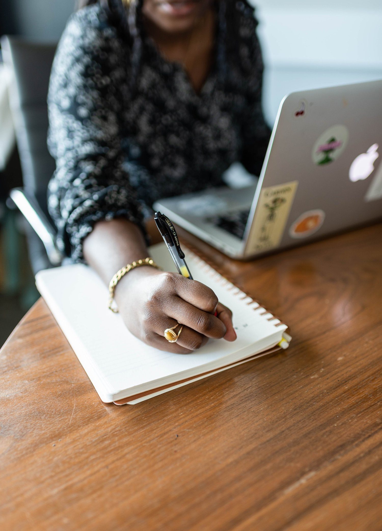 Hands writing in a notebook beside a laptop